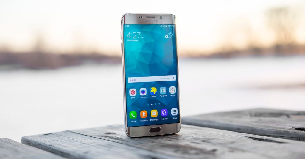 Samsung smartphone placed on a wooden surface outdoors during sunset.
