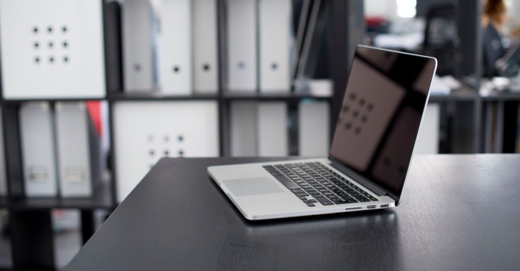 MacBook Pro displayed on a minimalist office desk with shelves in the background.
