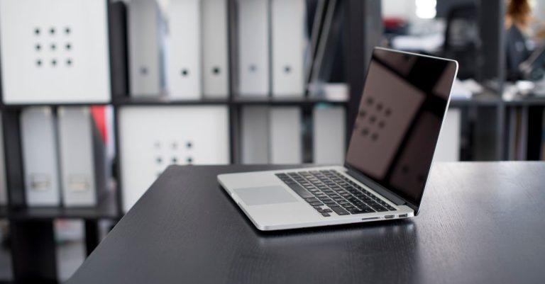 MacBook Pro displayed on a minimalist office desk with shelves in the background.