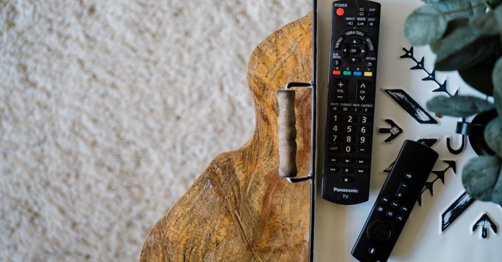 Two remote controls on a wooden tray with a metal surface and textured background.