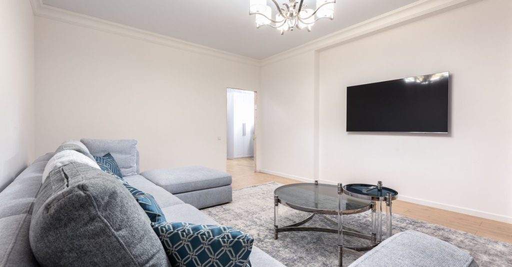 Contemporary room interior with couch and TV with black screen against tables under shiny chandelier in house