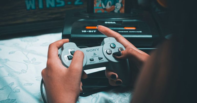 Close-up of hands holding vintage Sony controller with Sega Mega Drive in background.