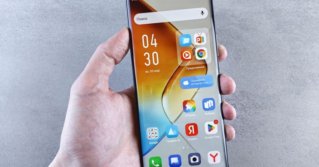 Close-up of a hand holding a smartphone displaying apps on the screen against a textured background.