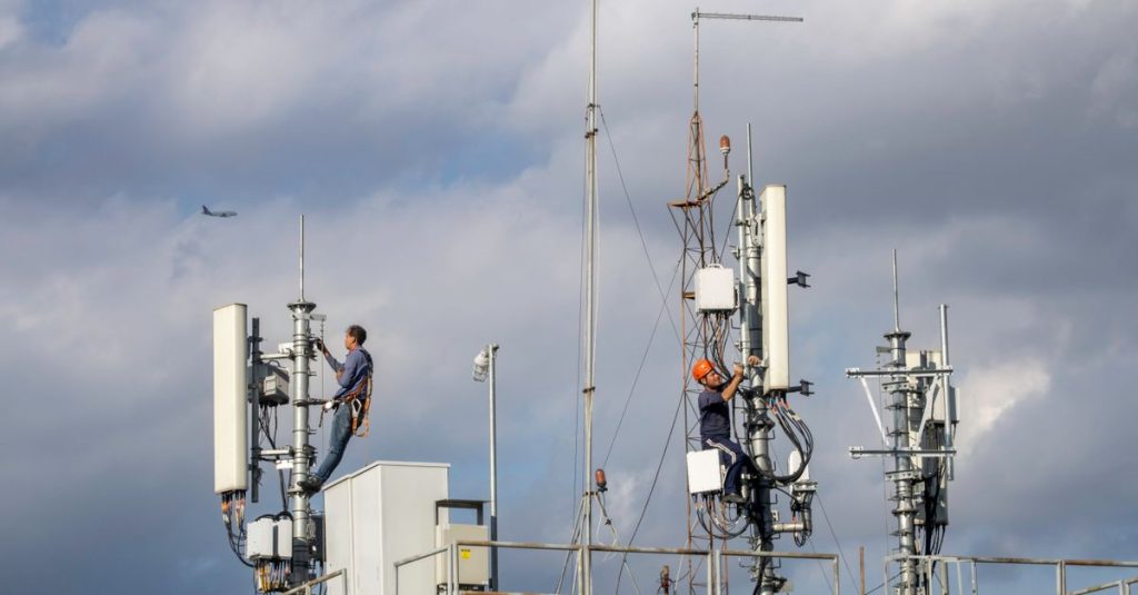 Two workers repairing a cellular tower against a cloudy sky, with an airplane in the background.