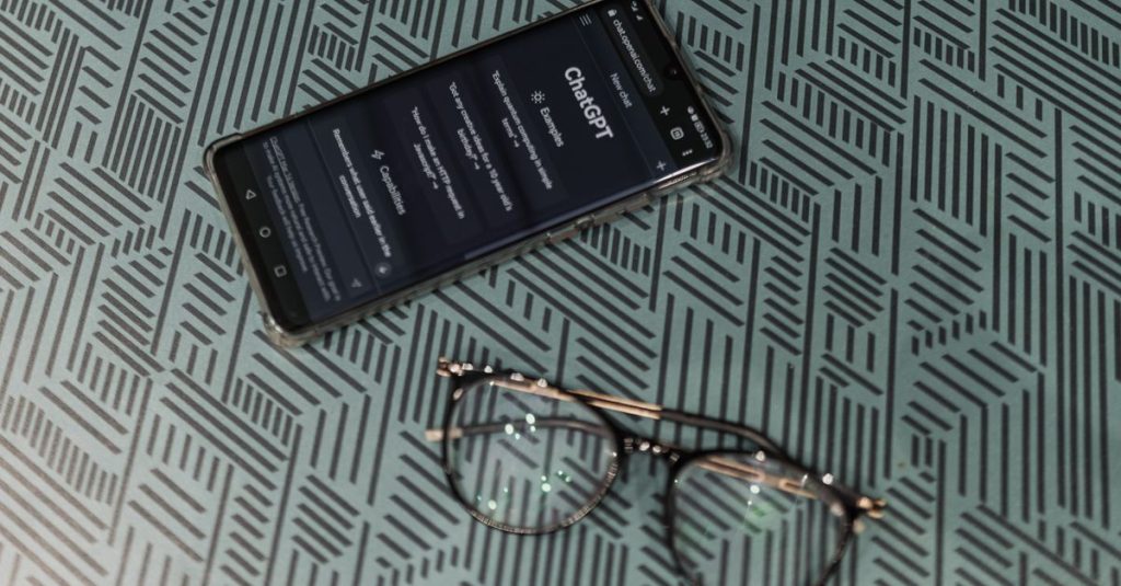 Close-up of smartphone displaying ChatGPT alongside eyeglasses on a patterned surface highlighting technology and style.