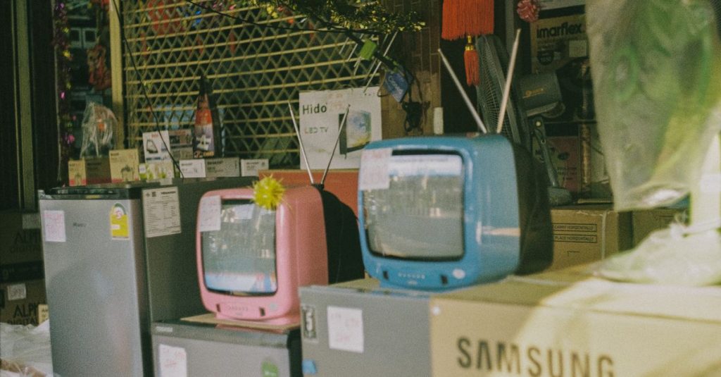 A storefront display featuring vintage televisions and home appliances on a sunny day in Bangkok.