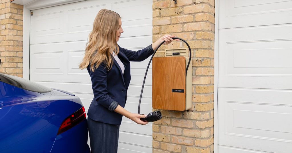 A woman using a home electric vehicle charger on a brick wall in a garage.