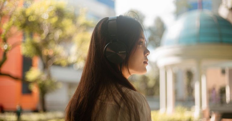Profile of a young woman enjoying music outdoors with headphones on a sunny day.
