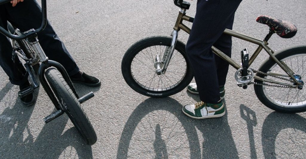 Two people with BMX bikes in an outdoor skatepark scene.