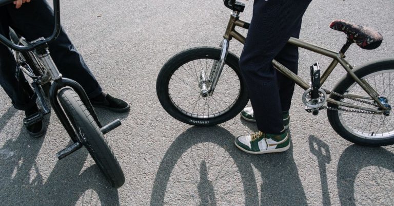 Two people with BMX bikes in an outdoor skatepark scene.