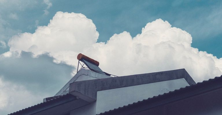 A building rooftop with a solar water heater set against a bright, cloud-filled sky.