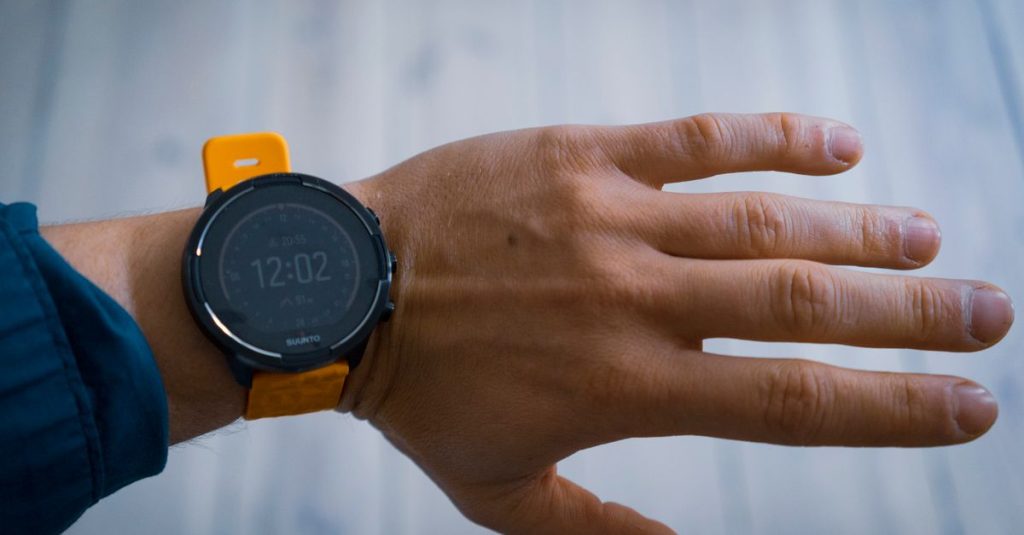 A close-up image of a smartwatch with a yellow strap worn on a wrist, displaying the time 12:02.