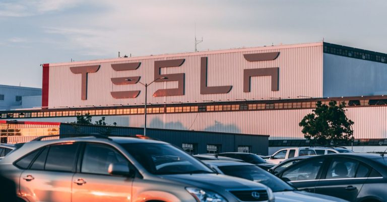 Tesla factory with parked cars during sunset, showcasing modern automotive industry vibes.