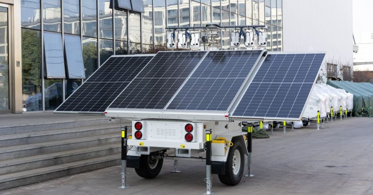 A mobile solar panel trailer parked outdoors by a modern building, showcasing renewable energy technology.