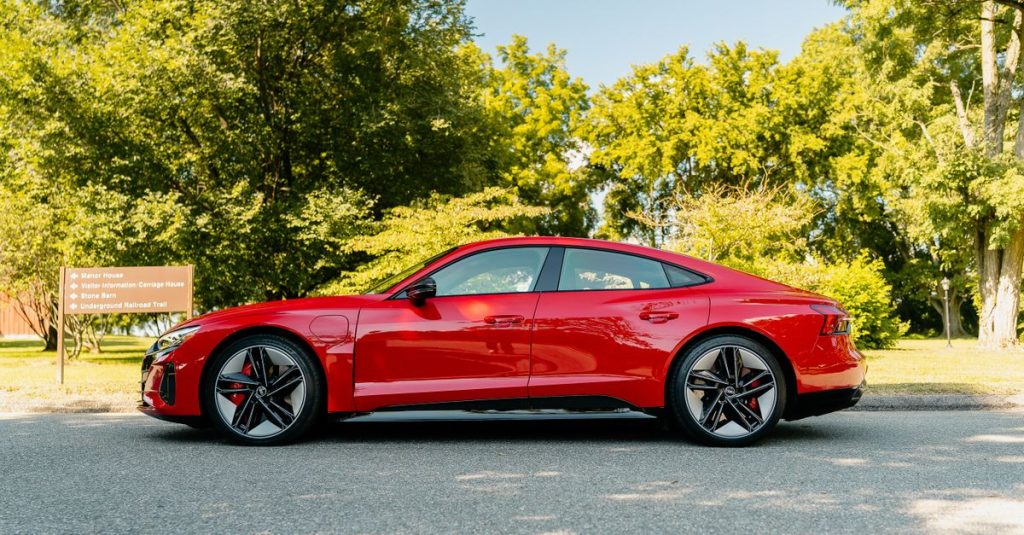 Side view of a luxury red sedan parked outdoors on a sunny day surrounded by greenery.
