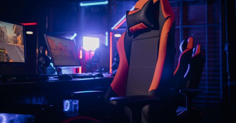 Modern gaming setup featuring a sleek chair and powerful PCs under neon lights.