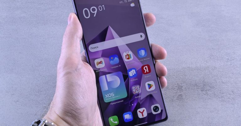 Close-up of a hand holding a smartphone displaying various apps on screen.