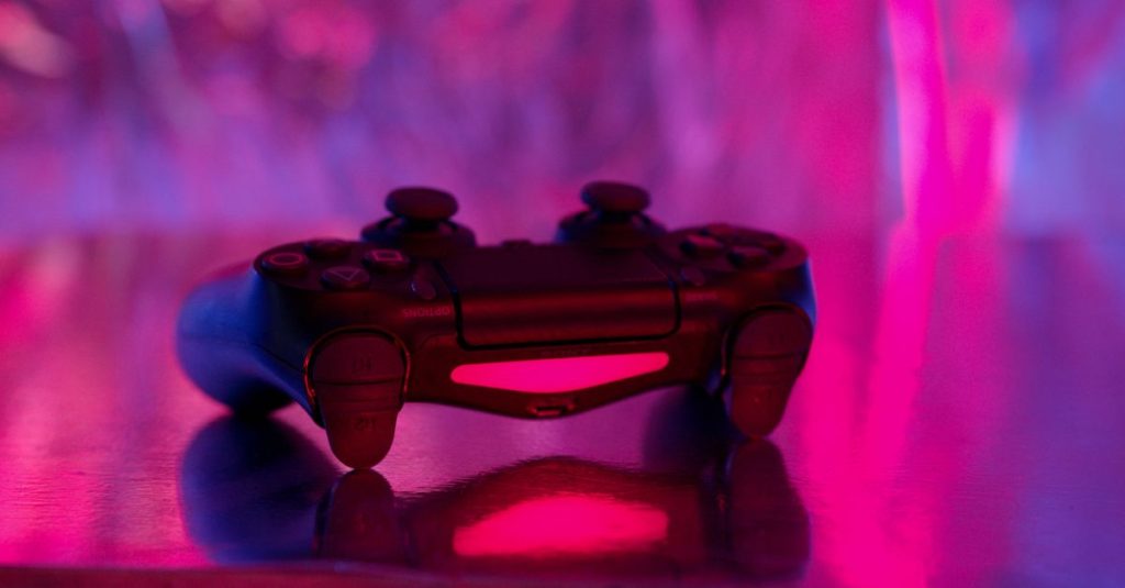 A wireless game controller in focus with a vibrant pink and purple neon background.