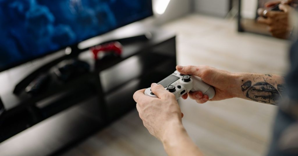 Person playing video games using a game controller indoors on a modern TV setup.