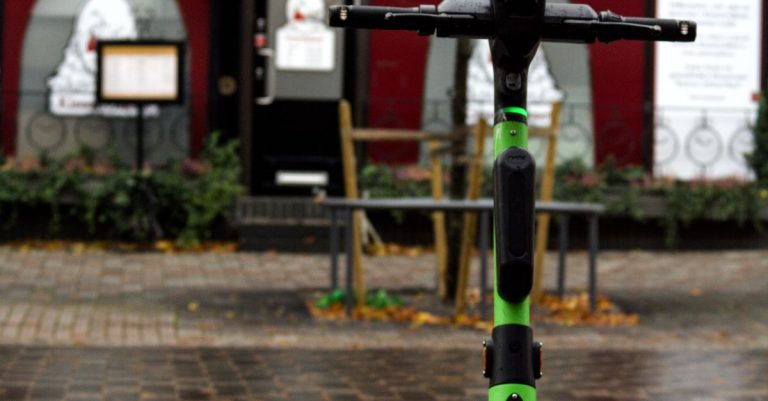 A green electric scooter strategically parked on a city sidewalk near a red storefront.